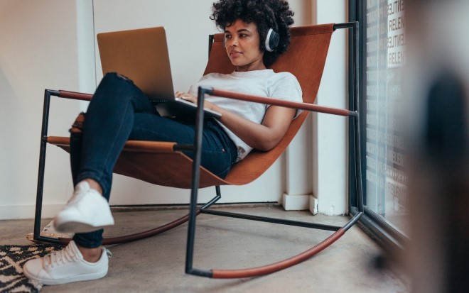 woman sitting in a chair looking at a laptop and wearing headphones